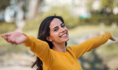 close-up-happy-woman-standing-with-open-arms-outdoors-smiling-camera
